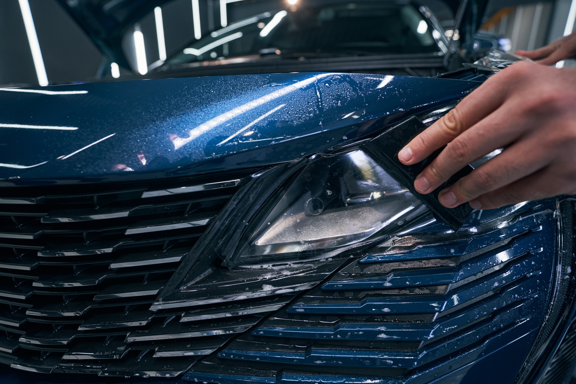 Closeup car service worker installing PPF with squeegee on headlight